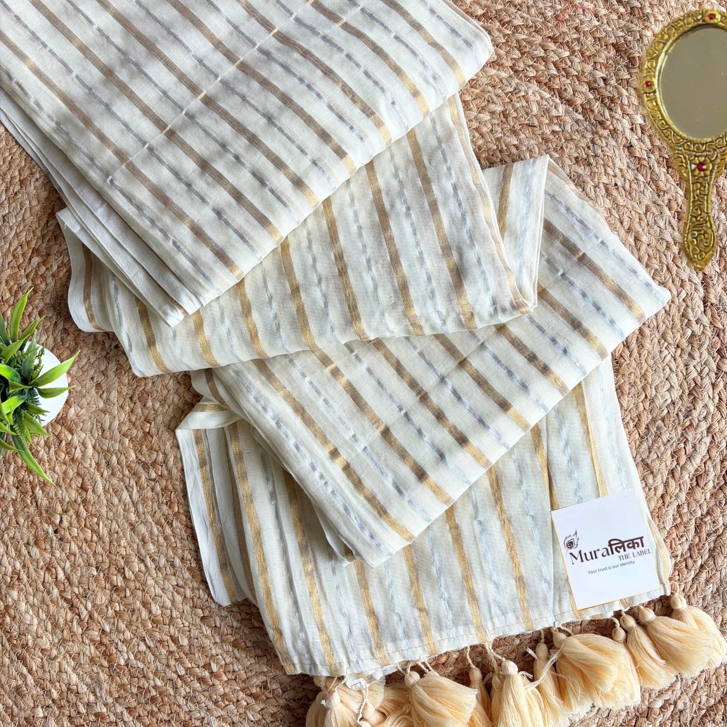 Ivory mulmul cotton saree striped in fine gold and silver zari, folded flat